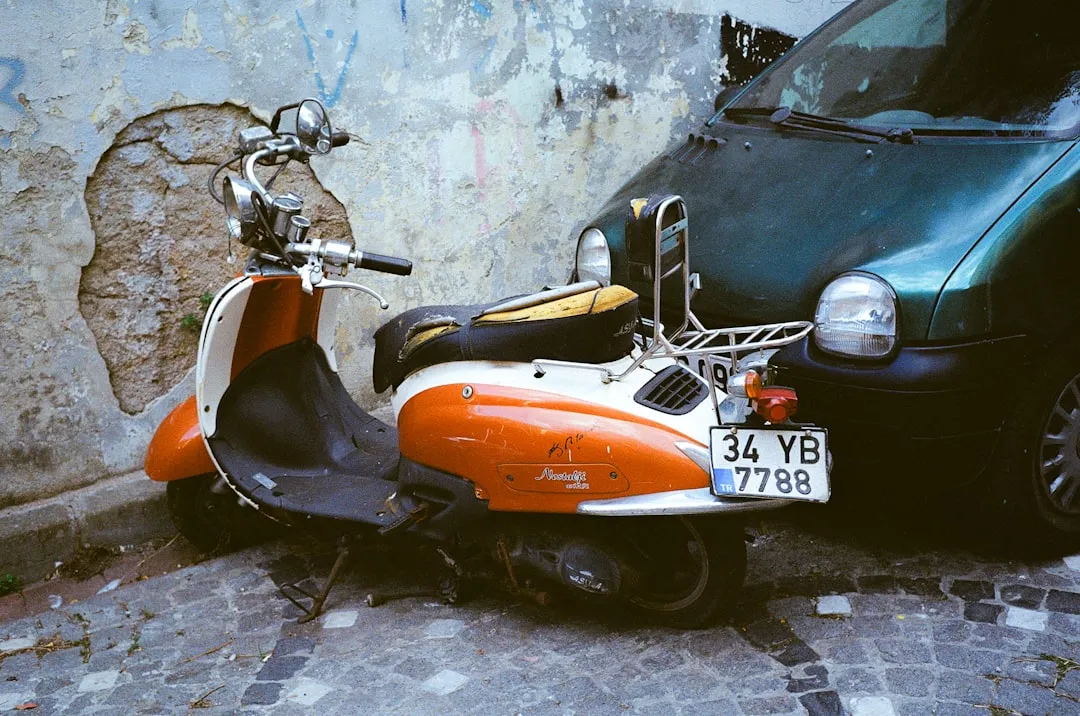 Orange and white scooter parked next to a car.