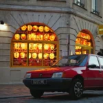 Red car parked outside a building with glowing windows.