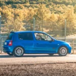 blue 5 door hatchback parked beside gray metal fence during daytime