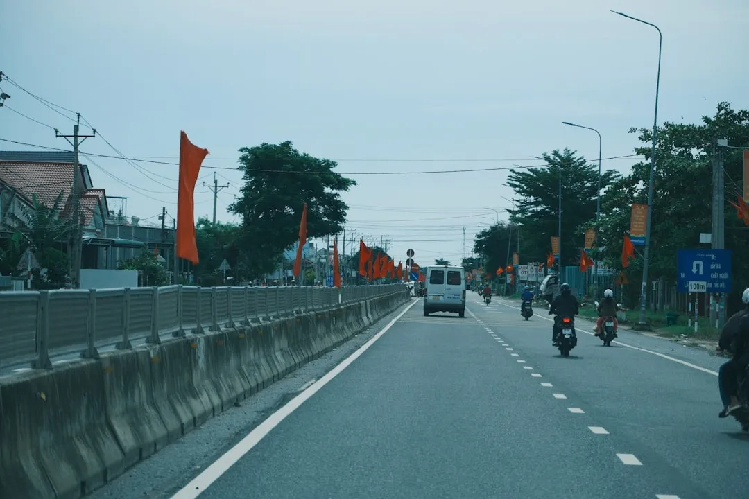 Orange flags line a road with vehicles and trees.